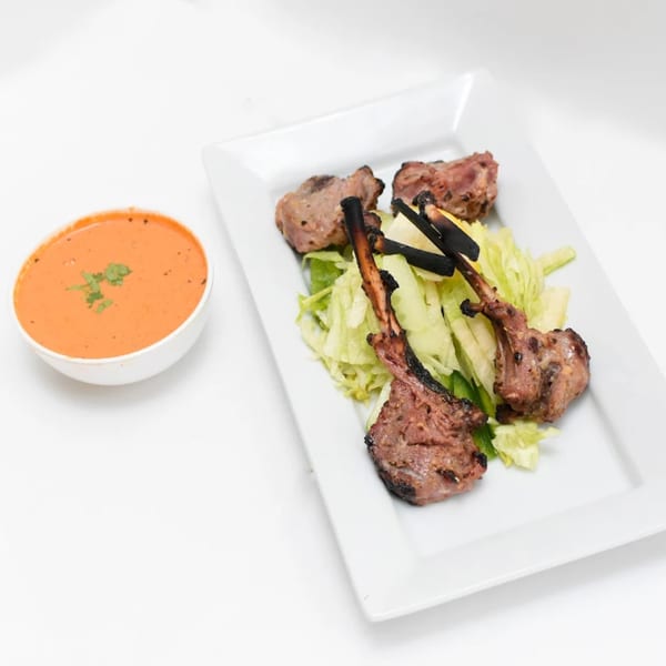 Indian lamb chops with charred green onions and lettuce, served with a side of orange sauce.