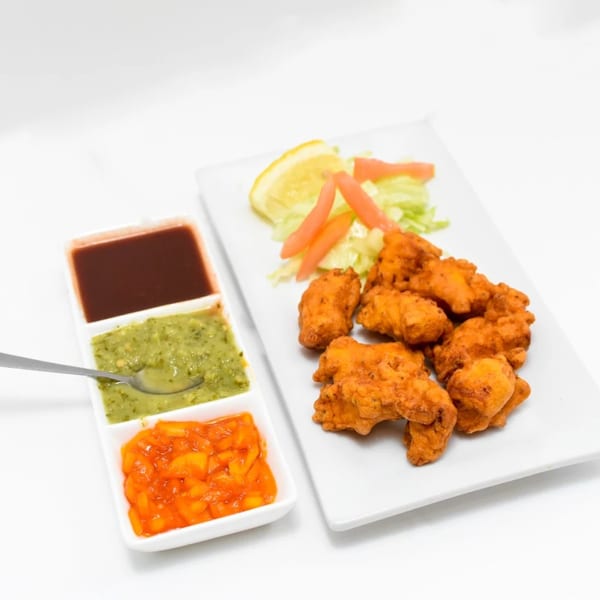 Shan-E-Panjab's Indian chicken pakora with salad and three dipping sauces on a white background.