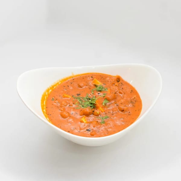 A white bowl filled with vibrant orange Indian curry, garnished with fresh green herbs.