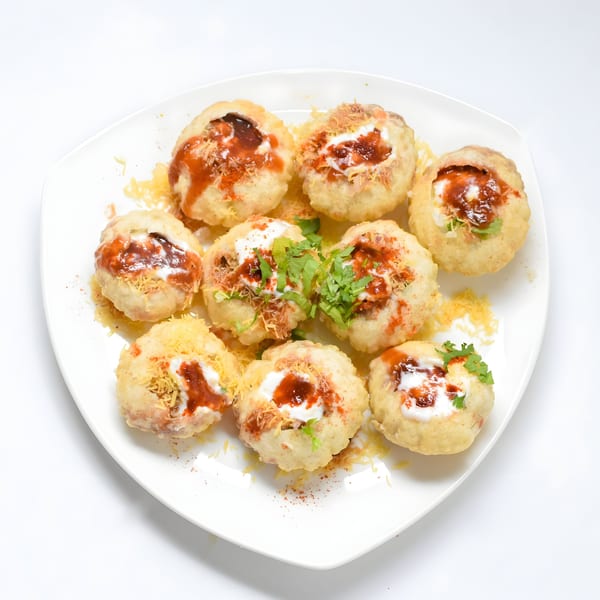 A white plate holds nine Indian pani puri, filled with sauces, spices, and cilantro.
